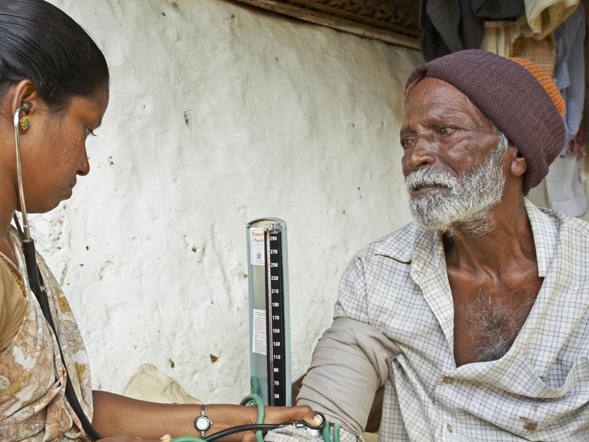 An elderly man having his blood pressure taken by a health worker.